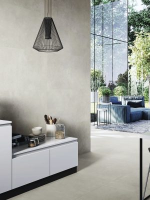 Urban Sand tile covers the walls and floor, seamlessly paired with a blue sectional couch and bathed in natural light from a high glass wall.